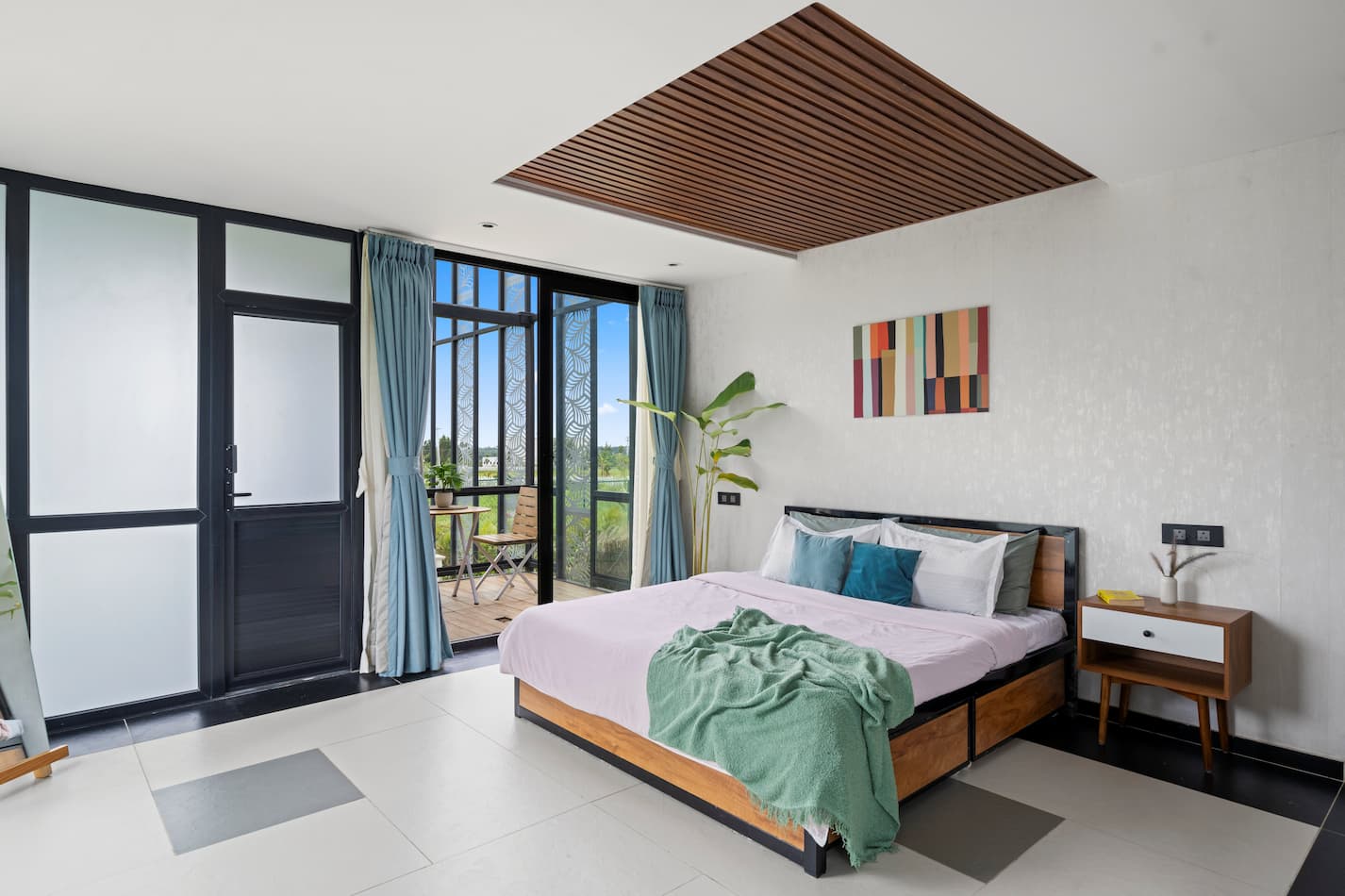 Master bedroom with balcony opening to forest views and teal curtains